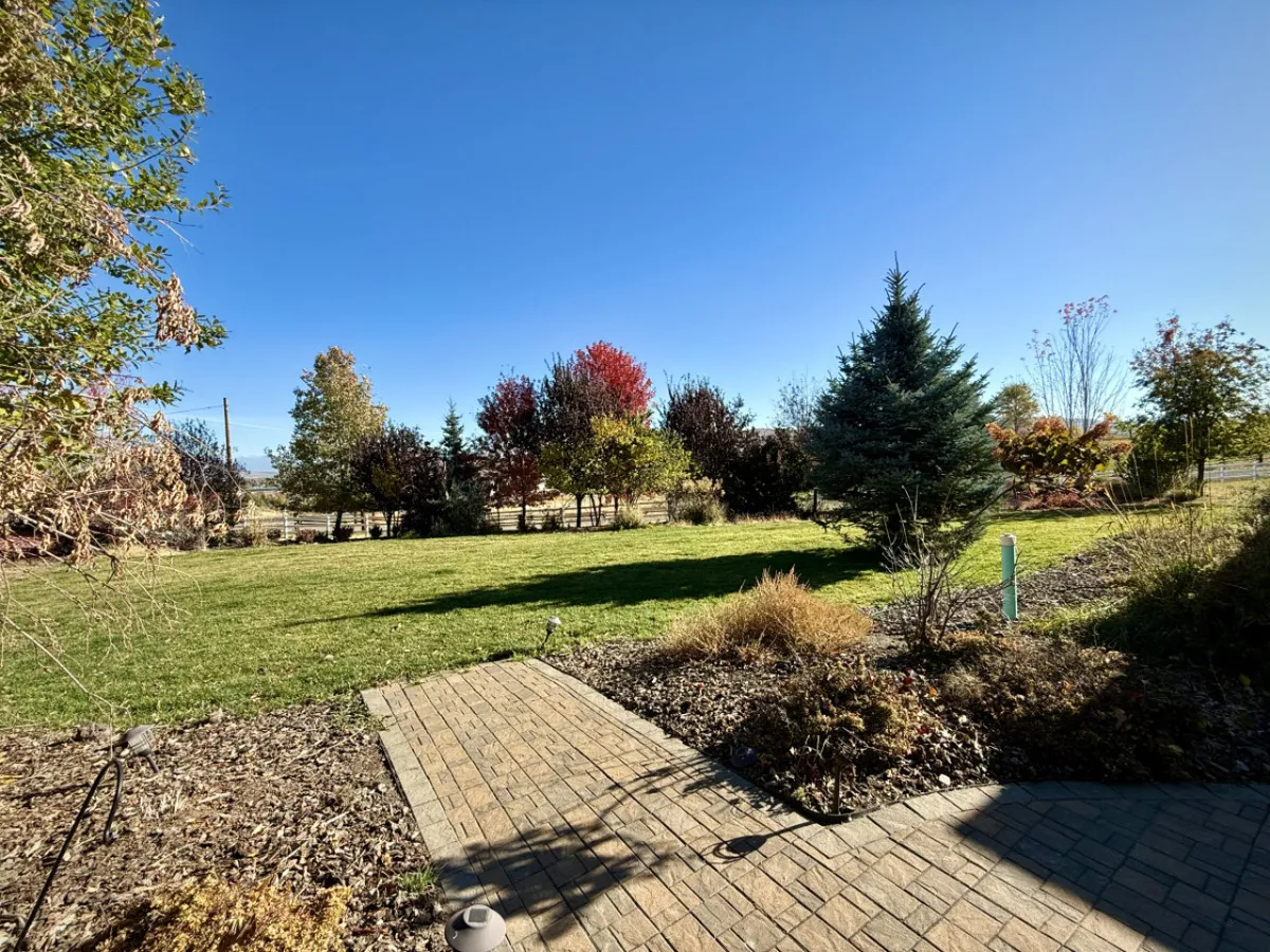 A wide, lush green lawn bordered by colorful trees and a paved pathway, offering a tranquil setting for gatherings, relaxation, or outdoor activities. The landscaping is well-maintained and inviting.