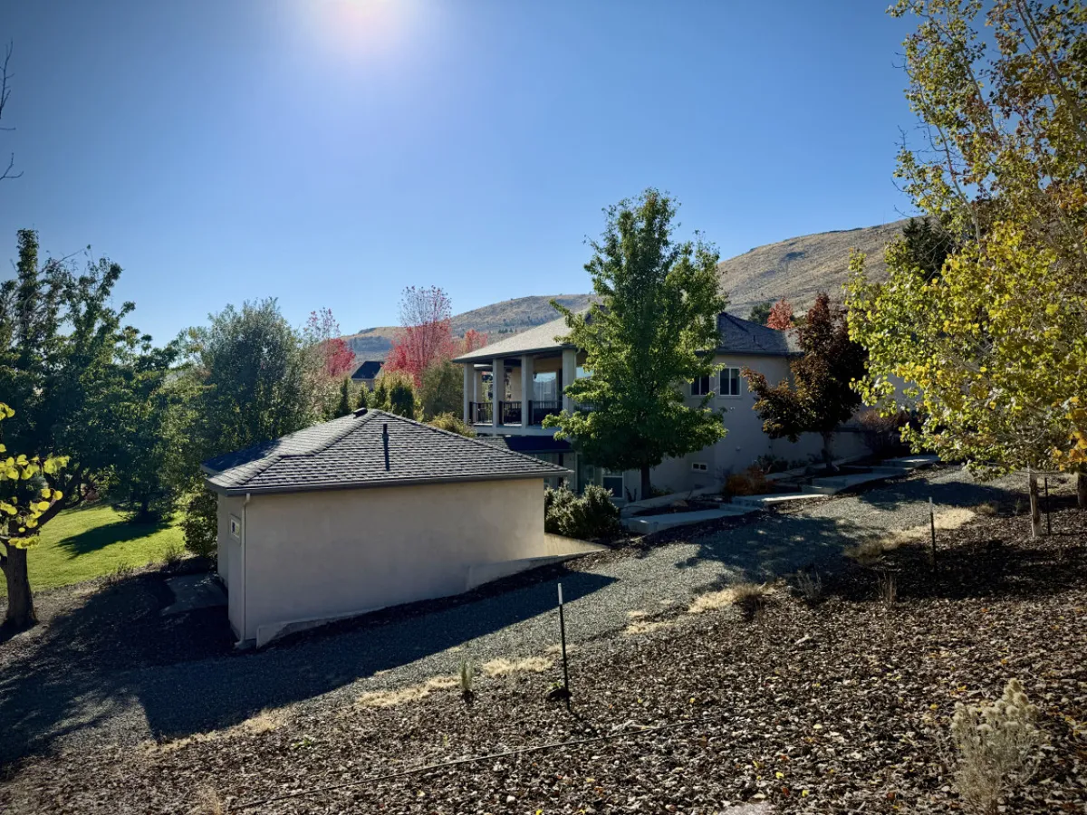 An exterior overview of the main house and an additional structure set amidst landscaped gardens, with mountains in the background. The spacious setting alludes to group gatherings, estate flexibility, and the beauty of the surrounding area.