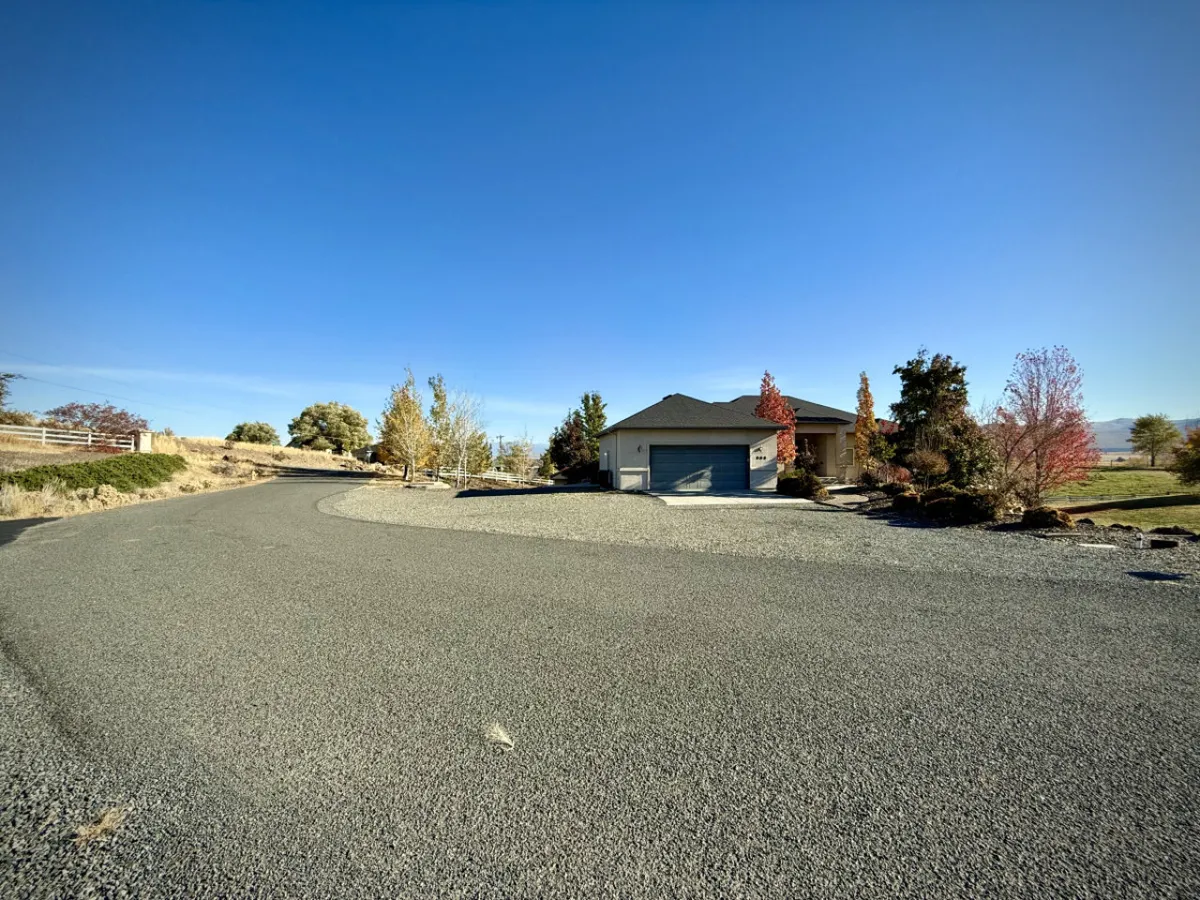 A wide, inviting shot of the house with a curved driveway, surrounded by mature trees and distant hills, ideal for gatherings or as a base for outdoor excursions.