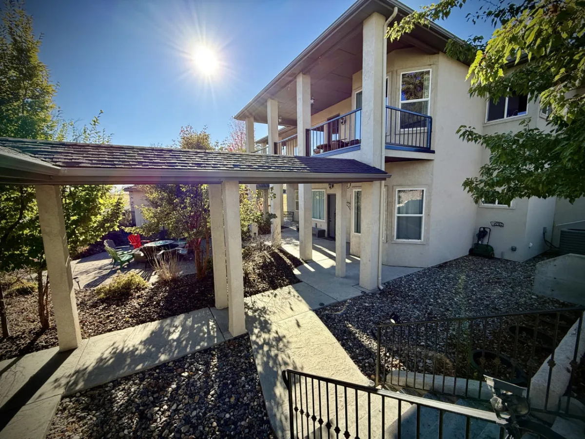 A sunlit porch with green chairs and blooming plants offers a cheerful, inviting spot for morning coffee or sunset relaxation. The outdoor seating and lush greenery evoke a sense of leisure and intimate moments shared in a tranquil setting.